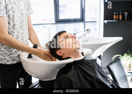 Parrucchiere capelli di lavaggio per il suo bel client. Barbiere al lavoro. Uomo al barbiere. Foto Stock