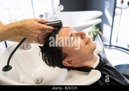 Vista di profilo di un giovane uomo di ottenere i suoi capelli lavati e la sua testa massaggiato in un salone di parrucchiere. Foto Stock