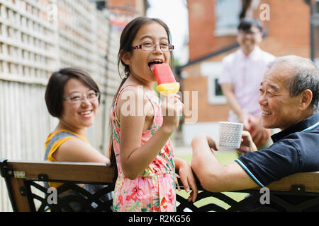 Ritratto ragazza felice di mangiare ghiaccio aromatizzato con multi-generazione famiglia nel cortile posteriore Foto Stock