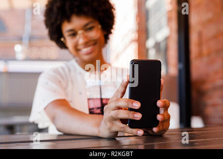 Close up donna mani di uno smartphone. Giovani blogger tenendo selfie con un drink sul tavolo. Foto Stock