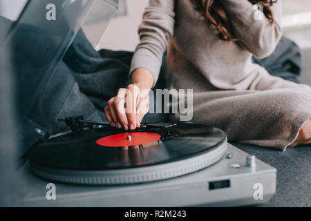 Ritagliato colpo di donna ascoltando musica con vinil record giocatore sul lettino a casa Foto Stock