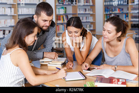 Felice giovani studenti universitari preparazione per l'esame insieme, brainstorming nella libreria Foto Stock