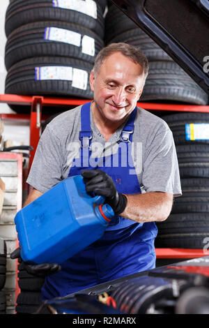 Esperto maturo mechanician auto cambio olio motore nel veicolo in negozio di riparazioni auto Foto Stock