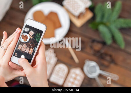 La ragazza fa una foto Flatley per reti sociali, il risultato del loro lavoro. Blog di blogger. Un sacco di biscotti allo zenzero. Natale umore, inverno mattina. Rami di abete e forme per la cottura. Foto Stock