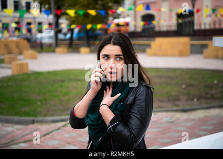 Scioccato giovane femmina adulta parlando al cellulare all'aperto sul banco di lavoro. Foto Stock