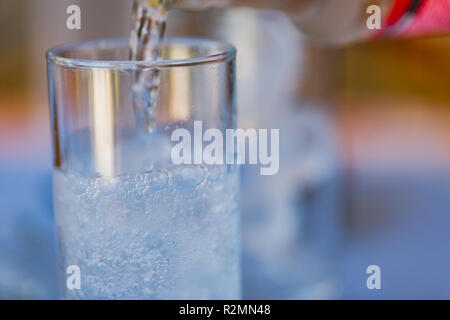 Primo piano versare acqua di bevanda fresca purificata dalla bottiglia sul tavolo nel soggiorno Foto Stock
