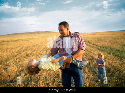 Uomo in un campo oscillando la sua giovane figlia intorno Foto Stock