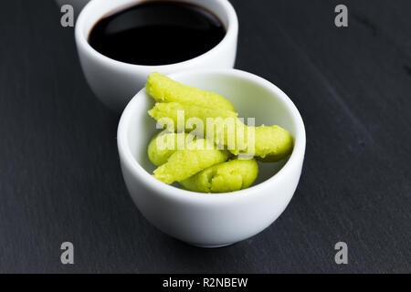 Rafano giapponese wasabi e salsa di soia in piccole ciotole bianco su nero ardesia cucina piastra. Cucina asiatica concetto astratto. Foto Stock