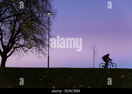 Persona escursioni in bicicletta di notte. Ciclista in sella ad una bicicletta di un passato via la luce e gli alberi in autunno, Nottingham, Inghilterra, Regno Unito Foto Stock