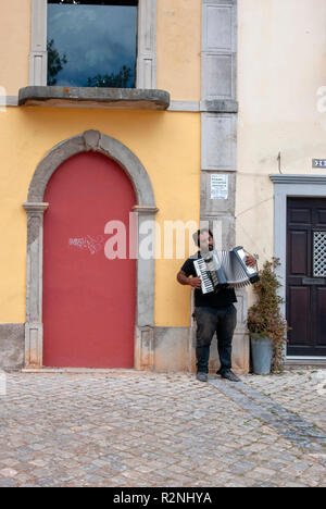 Suonatore ambulante Poruguese suonare la fisarmonica in strada di ciottoli Tavira portogallo dark scuoiate uomo portoghese con i capelli neri barba musicista suonatore ambulante mendicante musicista di strada Foto Stock