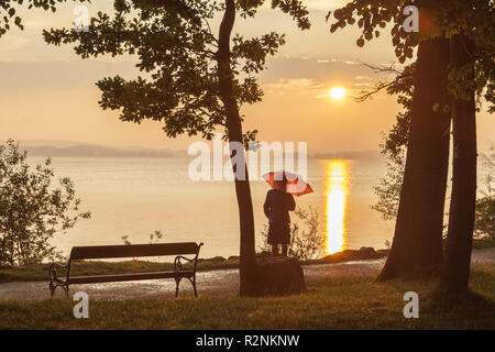 Donna sulla riva a Chiemsee durante il tramonto, a Übersee, Chiemgau, Alta Baviera, Baviera, Germania meridionale, Germania, Europa Foto Stock