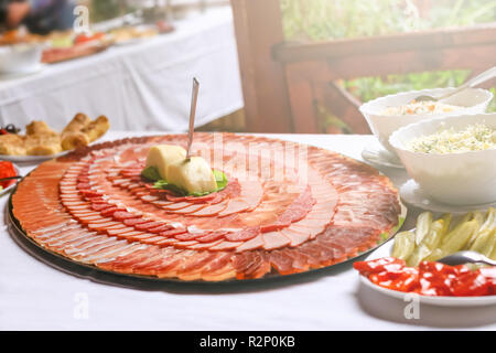 Deliziosa fette di carne di maiale, carne secca decorate in cerchi sul piatto di grandi dimensioni. Grande piatto con fette di carne su un matrimonio. Foto Stock