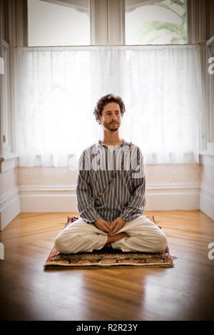 Metà di uomo adulto seduto in un yoga pone sul pavimento di una casa. Foto Stock