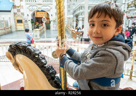 Un felice giovane ragazzo a cavallo su un merry-go-round. Foto Stock