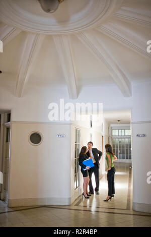 I giovani adulti business persone che parlano in un edificio per uffici in corridoio. Foto Stock