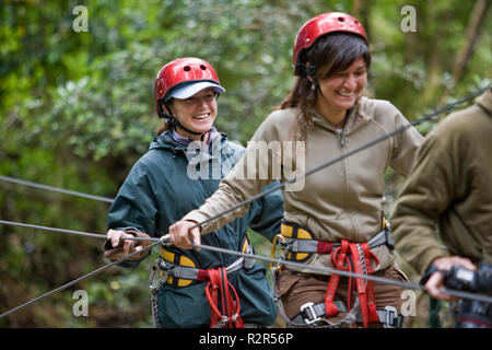 Due giovani donne di camminare su una tavola di legno ponte di sospensione in una foresta. Foto Stock
