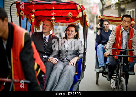 Turisti sorridente di equitazione in pedicabs lungo una strada di città. Foto Stock