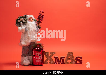 Santa Claus giocattolo in piedi accanto ad un Natale di legno segno di testo. Lo sfondo arancione con copia spazio Foto Stock