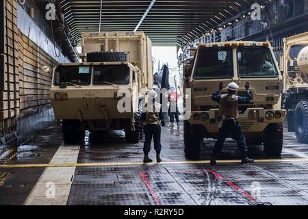 Le ACQUE AL LARGO DELLA COSTA DI SAIPAN (nov. 08, 2018) segnale di marinai di apparecchiature pesanti dal Guam Guardia Nazionale, 1224 Engineering Support Company, per spostarsi all'interno del pozzo del ponte della amphibious dock landing ship USS Ashland (LSD 48) per il supporto della difesa alle Autorità civili (DSCA) gli sforzi sull'isola di Saipan. Marinai e Marines dalla Ashland, assegnato al comandante, squadrone anfibio 11, sono fornendo il Dipartimento della Difesa sostegno alla Repubblica della Mariana Islands settentrionale' civile e funzionari locali come parte del FEMA-supportato Typhoon Yutu gli sforzi di recupero. Foto Stock