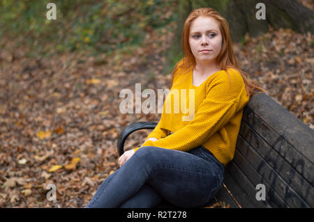 Un modello di donna seduta su una panchina nel parco di Norfolk in autunno Foto Stock