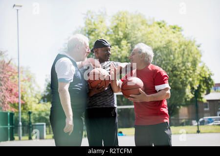 Active senior uomini amici giocare a basket nel soleggiato parco Foto Stock