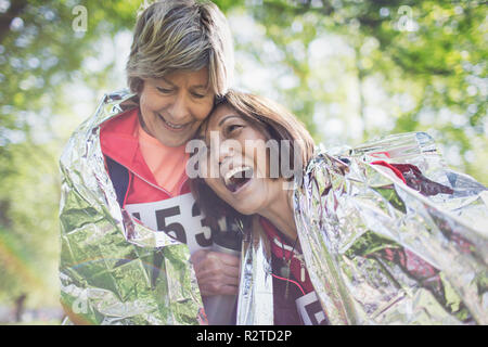 Felice active senior donne amici abbracciando dopo gara sportiva, avvolto in una coperta termica Foto Stock