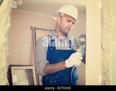 L uomo nel casco è segatura di parete con una sega circolare in mani. Foto Stock
