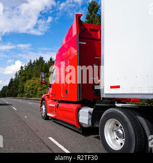 Rosso brillante cofano americano moderno long haul big rig semi carrello con cabina alta e dry van semi rimorchio trasporto commerciale cargo in movimento sul wi Foto Stock