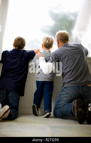 Metà di uomo adulto che guarda fuori della finestra con i suoi due figli. Foto Stock