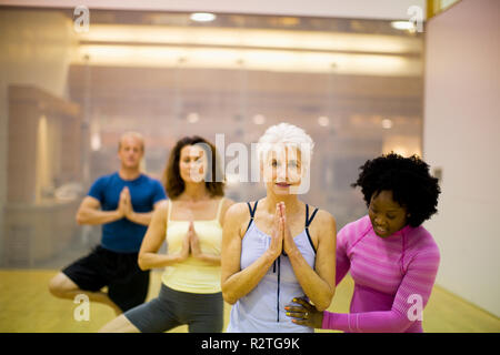 Sorridente giovane donna assistere un senior donna con il suo yoga pone all'interno di uno studio. Foto Stock
