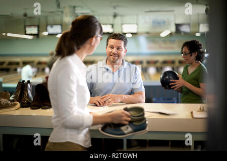 Sorridente metà uomo adulto verificando un paio di scarpe da bowling a una pista da bowling. Foto Stock