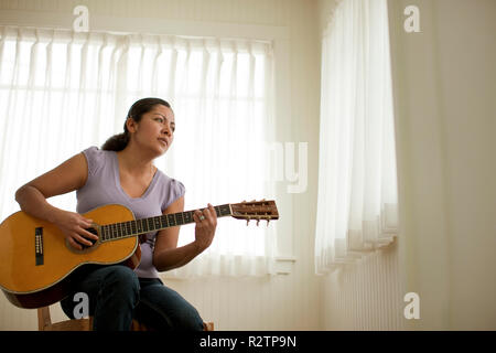 Giovane donna suonare la chitarra acustica e guardando fuori dalla finestra Foto Stock
