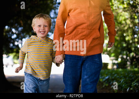 Padre e figlio tenendo le mani mentre correndo giù per la strada insieme. Foto Stock