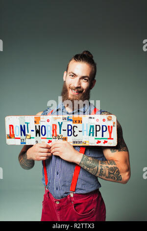 Ritratto fiducioso hipster man holding non preoccupatevi di essere felice di targhe Foto Stock