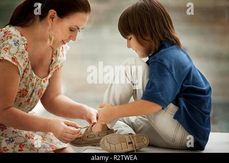 Middle-Aged madre aiuta il suo giovane figlio a legare il suo lacci delle scarpe. Foto Stock