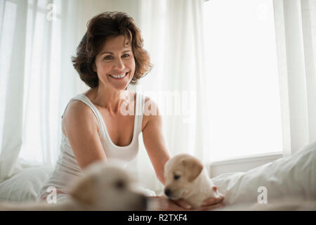 Sorridente metà donna adulta seduta sul letto con il Labrador cuccioli. Foto Stock