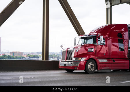 Perla brillante rosso moderno big rig semi carrello con forma geometrica e cabina alta per voli di lungo raggio guida su vasta ponte commercia di trasporto Foto Stock