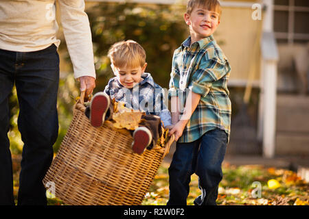 Ragazzo seduto sul cestello ed essendo portato da suo fratello e del nonno. Foto Stock