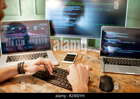 Programmatore di giovani la scrittura di un codice di programma seduta sul posto di lavoro con tre monitor in ufficio Foto Stock
