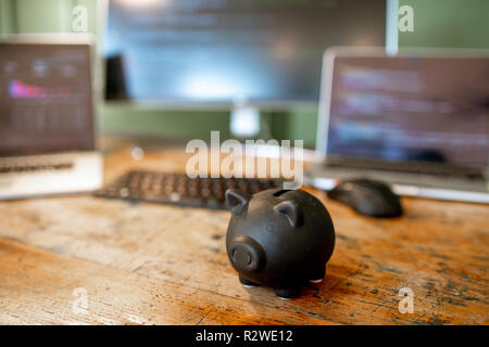 Piggybank nero sul tavolo con i computer sullo sfondo Foto Stock