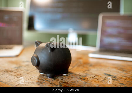 Piggybank nero sul tavolo con i computer sullo sfondo Foto Stock