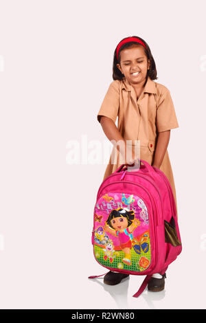 Bambina in uniforme scolastica raccolta un pesante sacco di scuola. Pune, Maharashtra Foto Stock