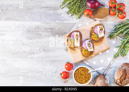 Sandwich con pezzi di aringhe marinate con cipolla rossa e senape francese, decorata limone e rosmarino. Vicino ristorante che serve, grigio chiaro wo Foto Stock