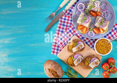 Sandwich con pezzi di aringhe marinate con cipolla rossa e senape francese, decorata limone e rosmarino. Vicino ristorante che serve, turchese woo Foto Stock