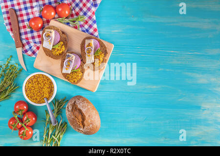 Sandwich con pezzi di aringhe marinate con cipolla rossa e senape francese, decorata limone e rosmarino. Vicino ristorante che serve, turchese woo Foto Stock