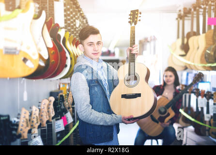 Positivo maschi e femmine di adolescenti scegliendo chitarre acustiche in guitar shop Foto Stock