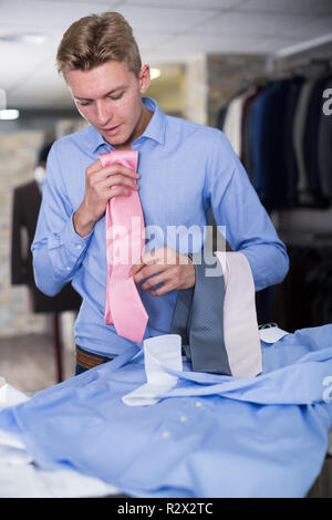 Maschio adulto acquirente in camicia scegliendo il tirante in negozio di abbigliamento Foto Stock