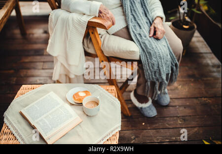 Una sezione mediana vista della donna anziana con un libro all'aperto su una terrazza in autunno. Foto Stock