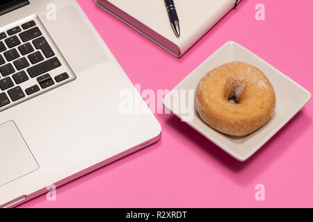 Rosa con desktop ciambella snack al fianco di laptop e notebook. Foto Stock