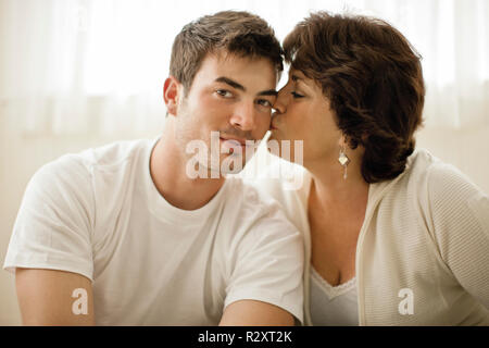 Ritratto di un giovane uomo baciato sulla guancia da sua madre. Foto Stock